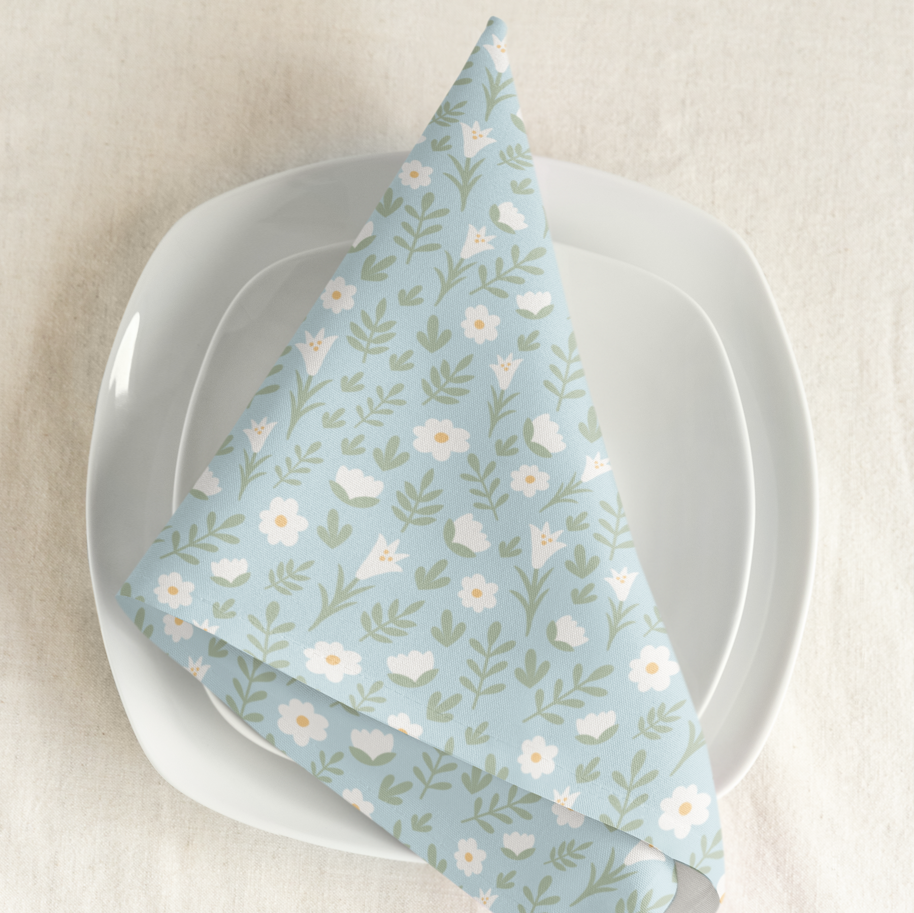 Light blue Easter Alleluia napkin with white floral design placed on a plate in a styled table setting.