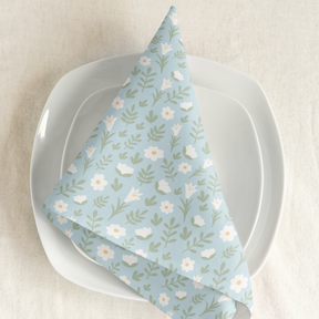 Light blue Easter Alleluia napkin with white floral design placed on a plate in a styled table setting.