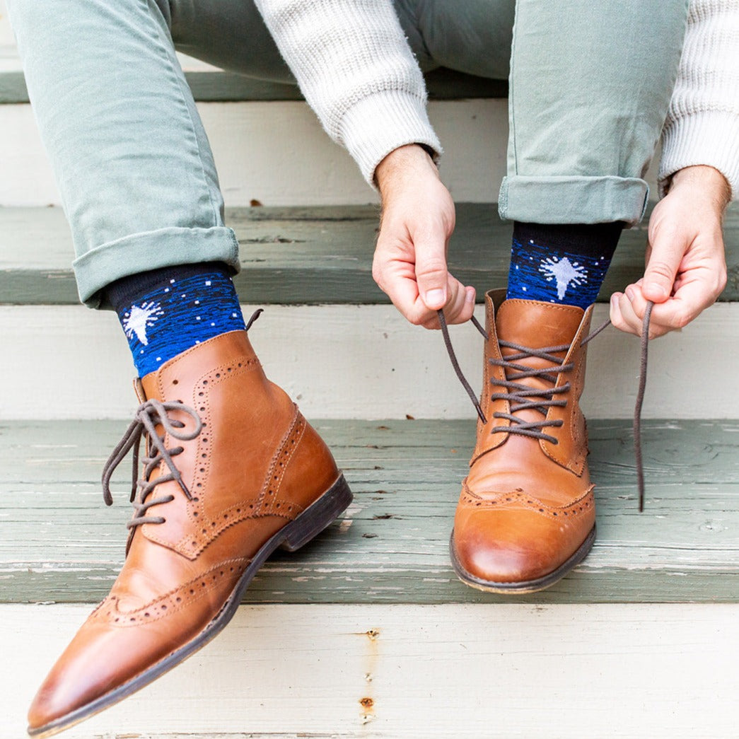 a person tying a pair of brown shoes wearing Three Wisemen socks