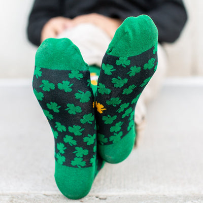 man sitting showing bottom of Green socks with green clovers and St. Patrick of Ireland